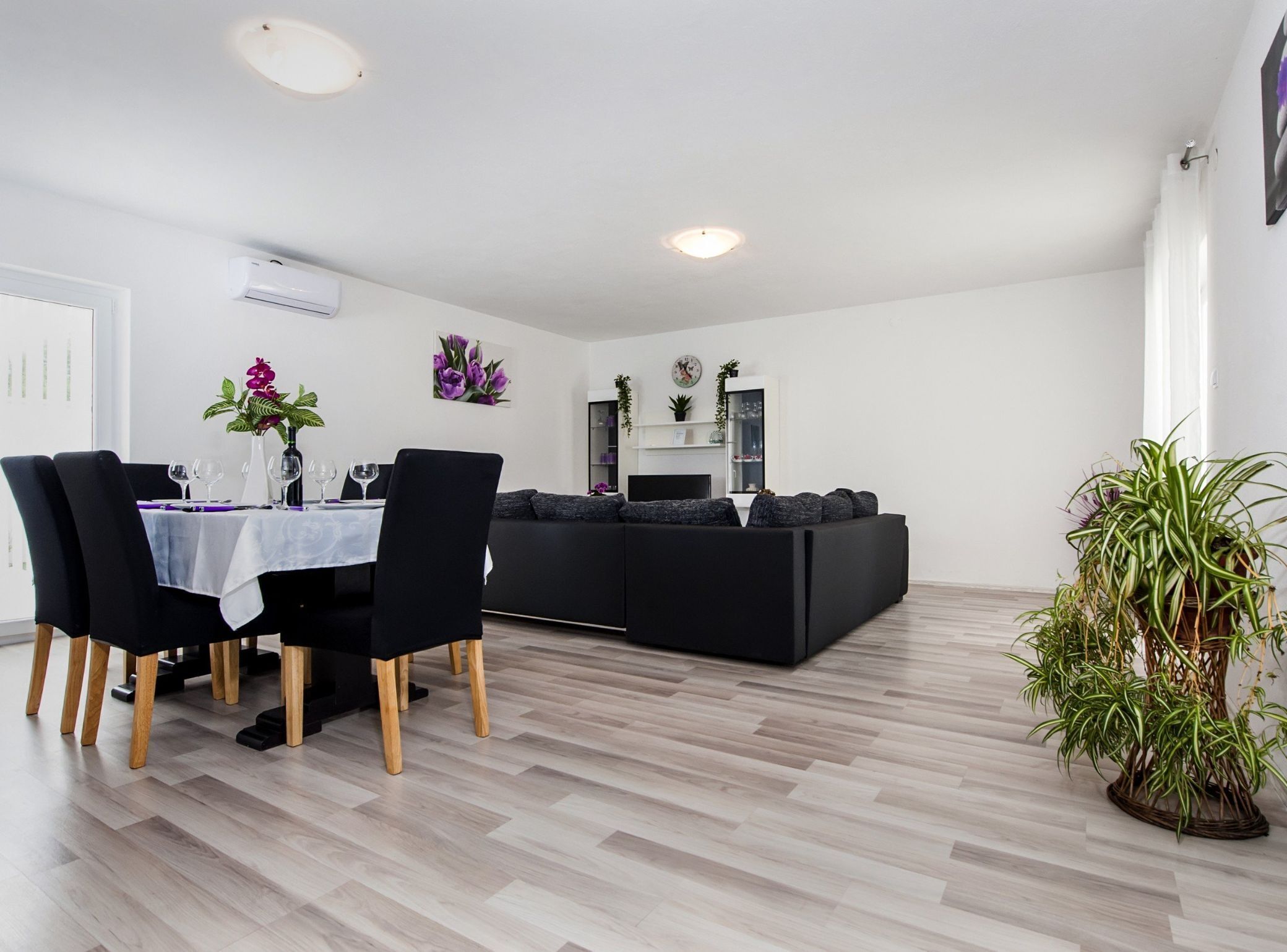 A modern living space with a dining area, black sofa, and potted plants.