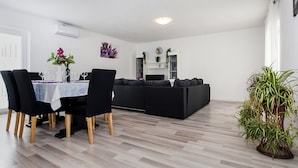 Un espacio habitable moderno con zona de comedor, sofá negro y plantas en macetas.