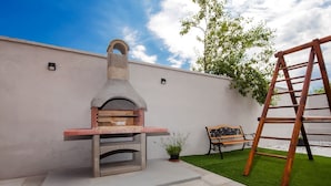 Un patio al aire libre con un horno de pizza de piedra, un banco de madera y una escalera.