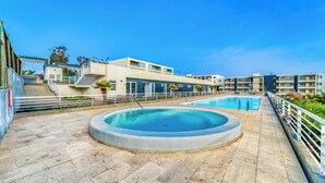 Piscina com design circular, escadaria para um andar superior e um edifício com varandas.