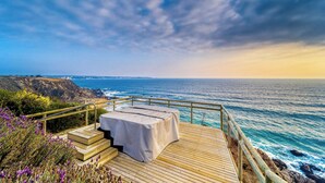Um deck de madeira com mesa e escadas com vista para o oceano.