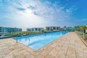 Una piscina rectangular con una escalera metálica en un lado, rodeada por un solárium de baldosas.