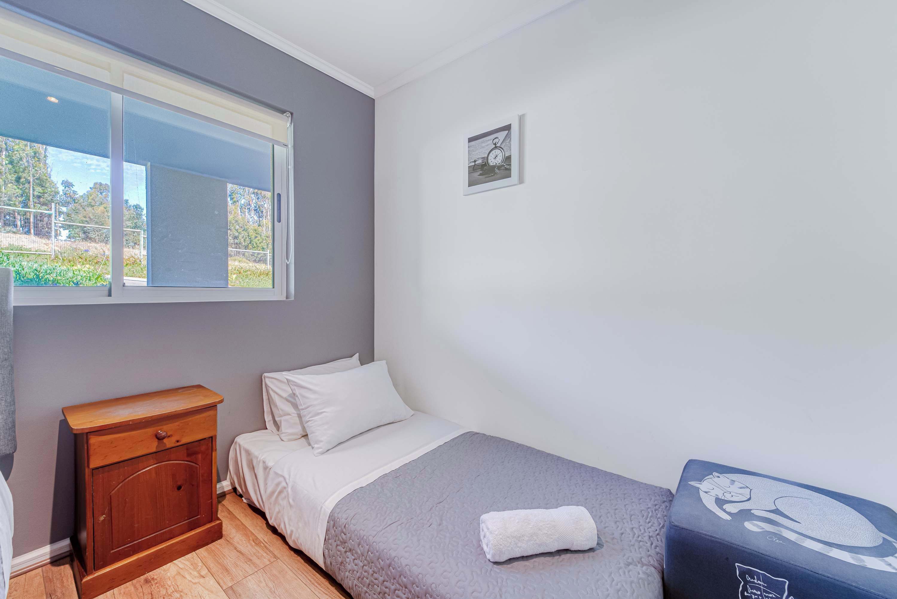 Quarto com uma cama, mesa de cabeceira, janela e um pequeno quadro na parede.