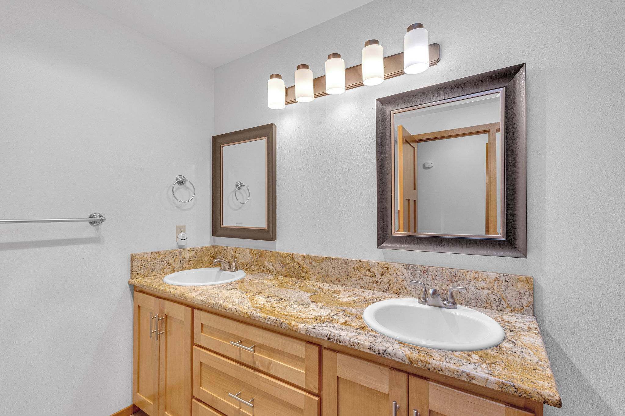 A bathroom with two sinks, wooden cabinets, a towel rack, and wall-mounted lighting.