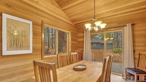 A wooden-paneled room with a dining table, chairs, a chandelier, and large windows. - Recently updated, great location, private hot tub! (Sunriver)