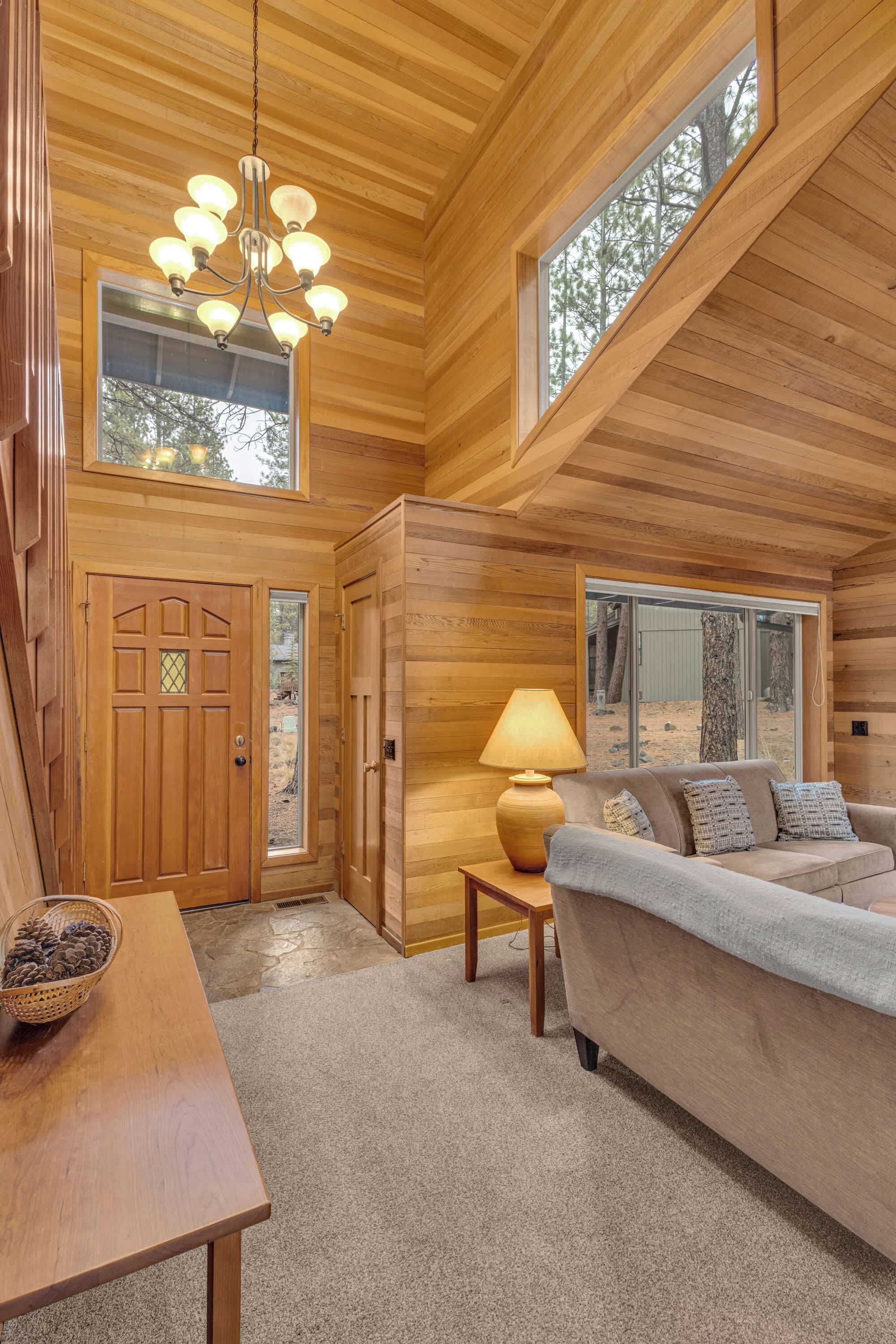 A spacious living area with a wooden ceiling, a large window, a sofa, a table, and a lamp.