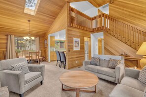 A spacious living area with a high ceiling, wooden walls, and a staircase leading to an upper level.