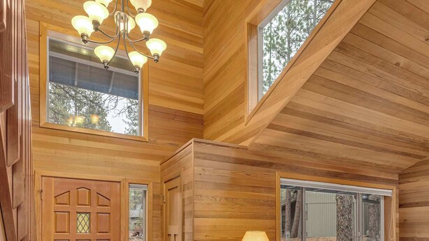 A cozy cabin interior with a wooden ceiling, a chandelier, a sofa, a lamp, and a door with a window. - Recently updated, great location, private hot tub! (Sunriver)