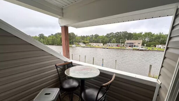 A covered outdoor area with a table and chairs, overlooking a body of water and a dock with boats. - Knot Four- Balcony View of ICW- Dog Friendly! (Coinjock)