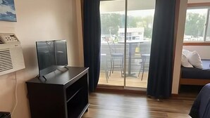 A hotel room with a sliding glass door to a balcony, a small TV on a black stand, and a bed with a blue cover. - Knot Four- Balcony View of ICW- Dog Friendly! (Coinjock)