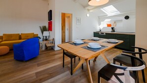 A modern living room with a wooden dining table, blue sofa, and a kitchen area with green cabinets and a skylight. - Radiant and Trendy Downtown Rovinj Apartment (Rovinj)