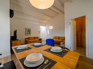 A dining area with a wooden table set for four, a sofa, and a television in the corner. - Radiant and Trendy Downtown Rovinj Apartment (Rovinj)