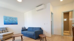 A living room with a blue sofa, a smaller sofa, two wooden side tables, and a wall-mounted air conditioner. - Sunny Rovinj Apartment With Sea View (Rovinj)