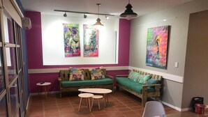 Ein gemütliches Wohnzimmer mit einem grünen Sofa, zwei kleinen Tischen und farbenfroher Kunst an den Wänden.
