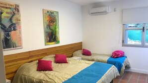 Ein Zimmer mit zwei Betten, jeweils mit einem Holz-Kopfteil, einem Fenster mit Blick auf Grünflächen und einer Klimaanlage an der Wand.
