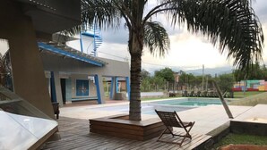 Eine Holzterrasse mit Palme, Pool und Gebäude mit blauen Akzenten.