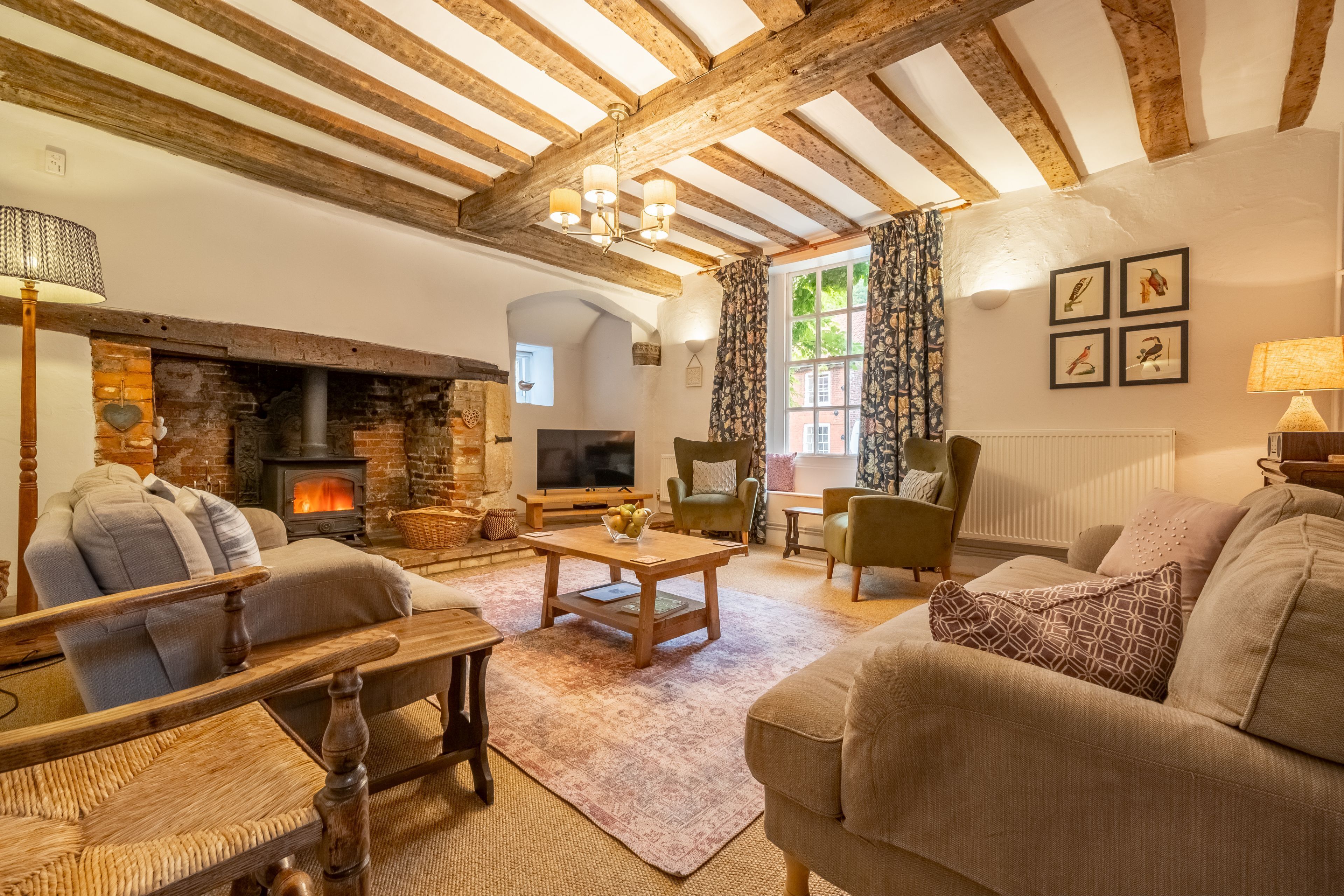 A cozy living room with exposed wooden beams, a fireplace, comfortable seating, and a television.