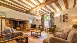 A cozy living room with exposed wooden beams, a fireplace, comfortable seating, and a television.