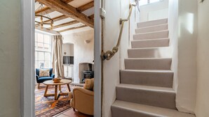 A staircase with a rope handrail, a living room with a sofa, a table, and a patterned rug.