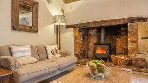A cozy living room with a sofa, a wooden coffee table with fruit, a fireplace, and a mirror on the wall.