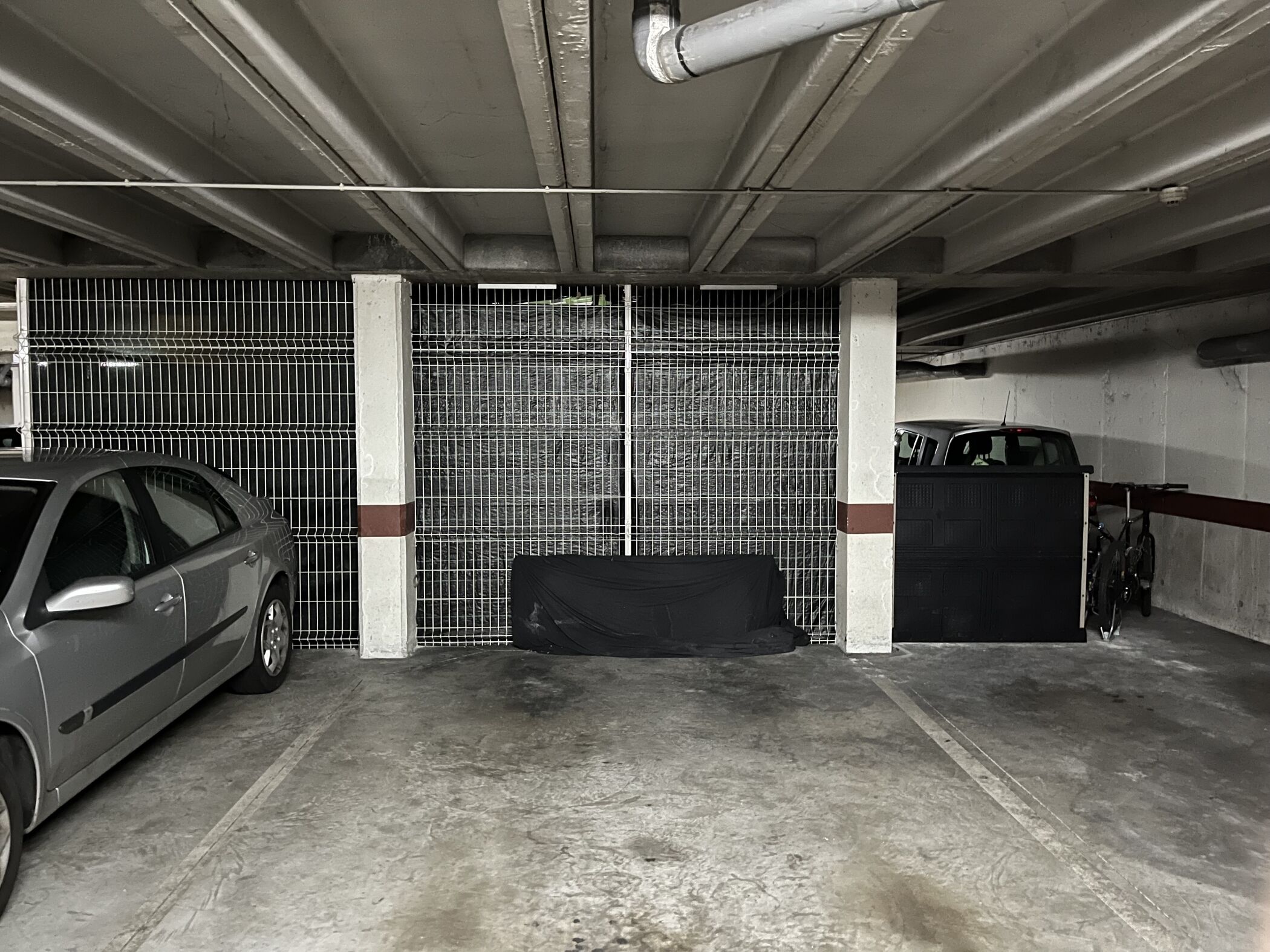 A parking garage with a car parked near a gated area, concrete floors, and metal railings.
