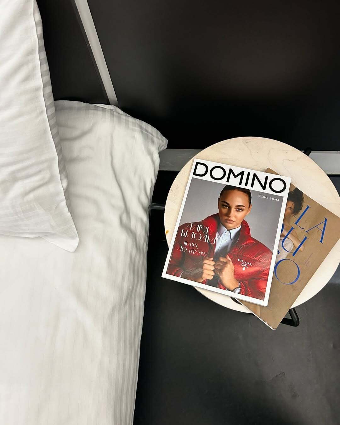 A bed with white bedding and a magazine on a bedside table.