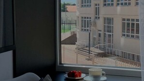 A room with a window overlooking a building with multiple windows and a staircase. There is a plate with red items and a cup on the windowsill.