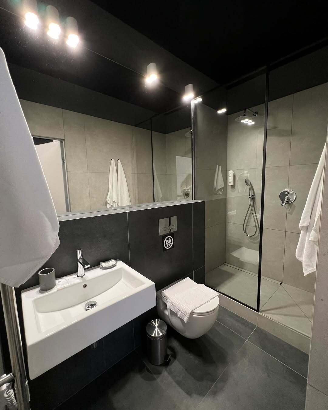 Un baño moderno con un espejo grande, un lavamanos, un inodoro y una zona de ducha.
