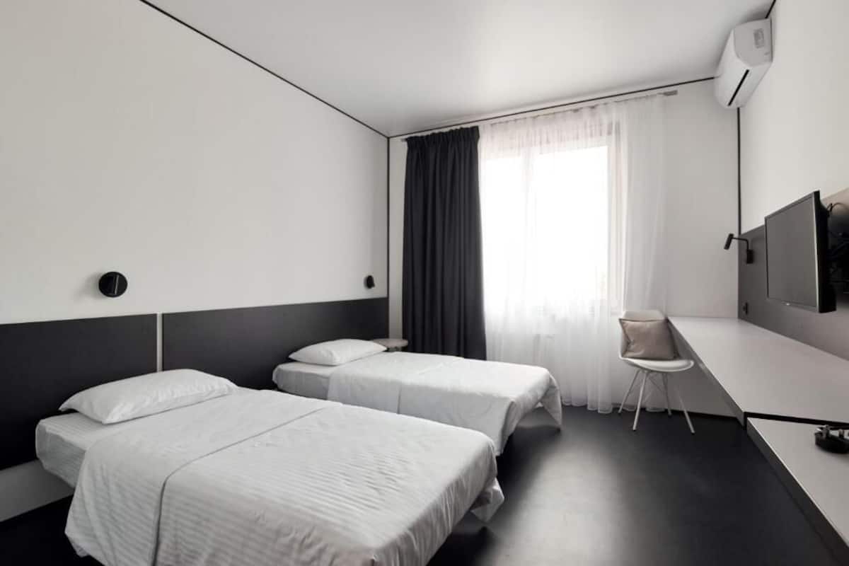 Een hotelkamer met twee eenpersoonsbedden, een bureau, een stoel, een televisie en een raam met gordijnen.