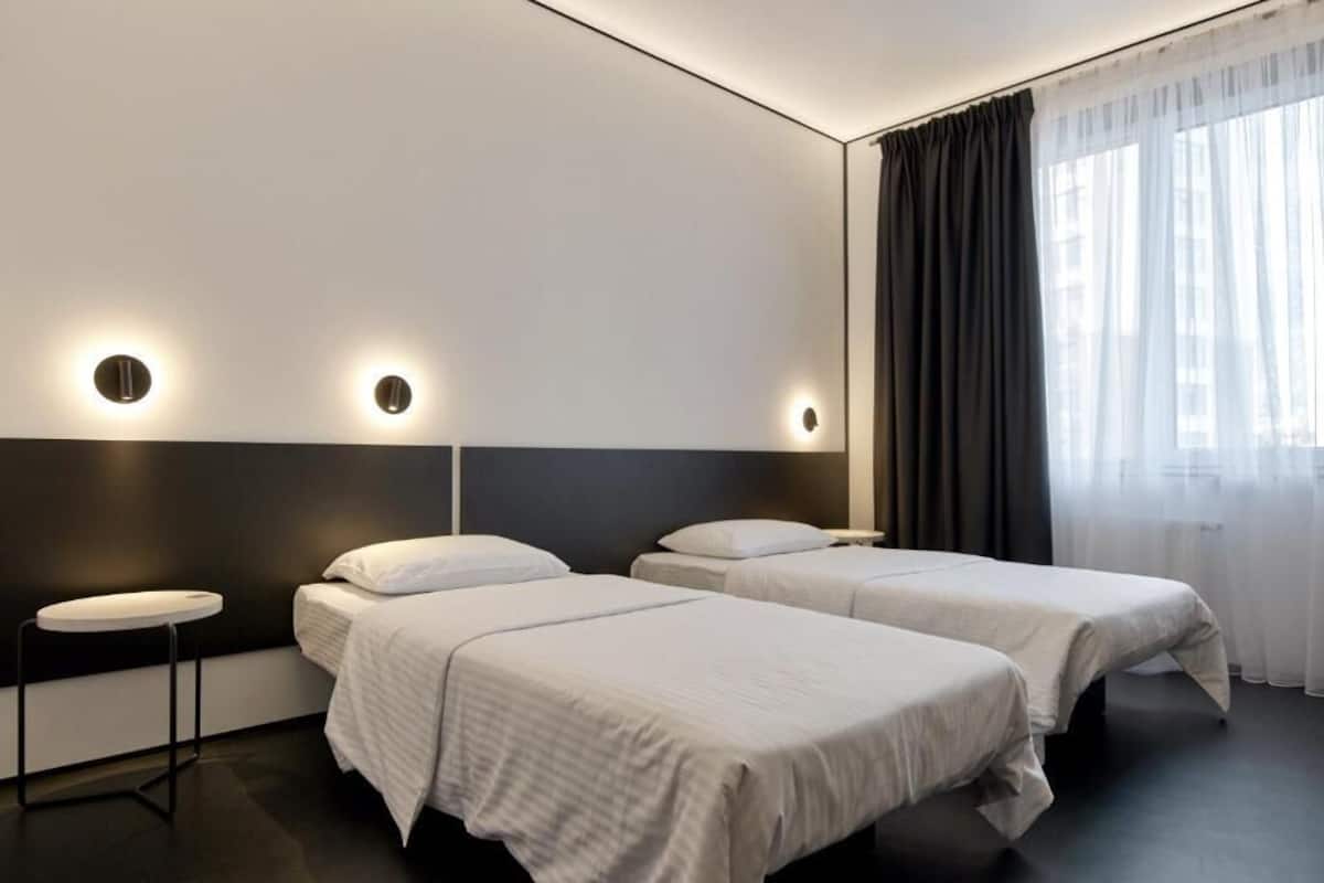 Een moderne hotelkamer met twee enkele bedden, een rond bijzettafeltje en een groot raam met dunne gordijnen.