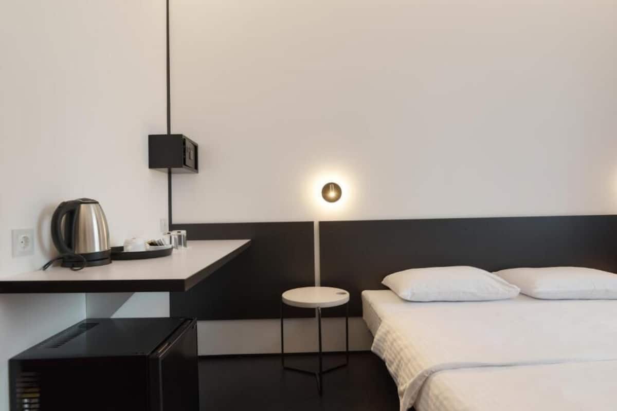 Een hotelkamer met een bed, nachtkastje, lamp en een kleine kitchenette.