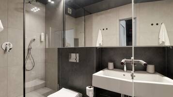A modern bathroom with a glass-enclosed shower, a white toilet, and a large mirror above a white sink with two faucets.