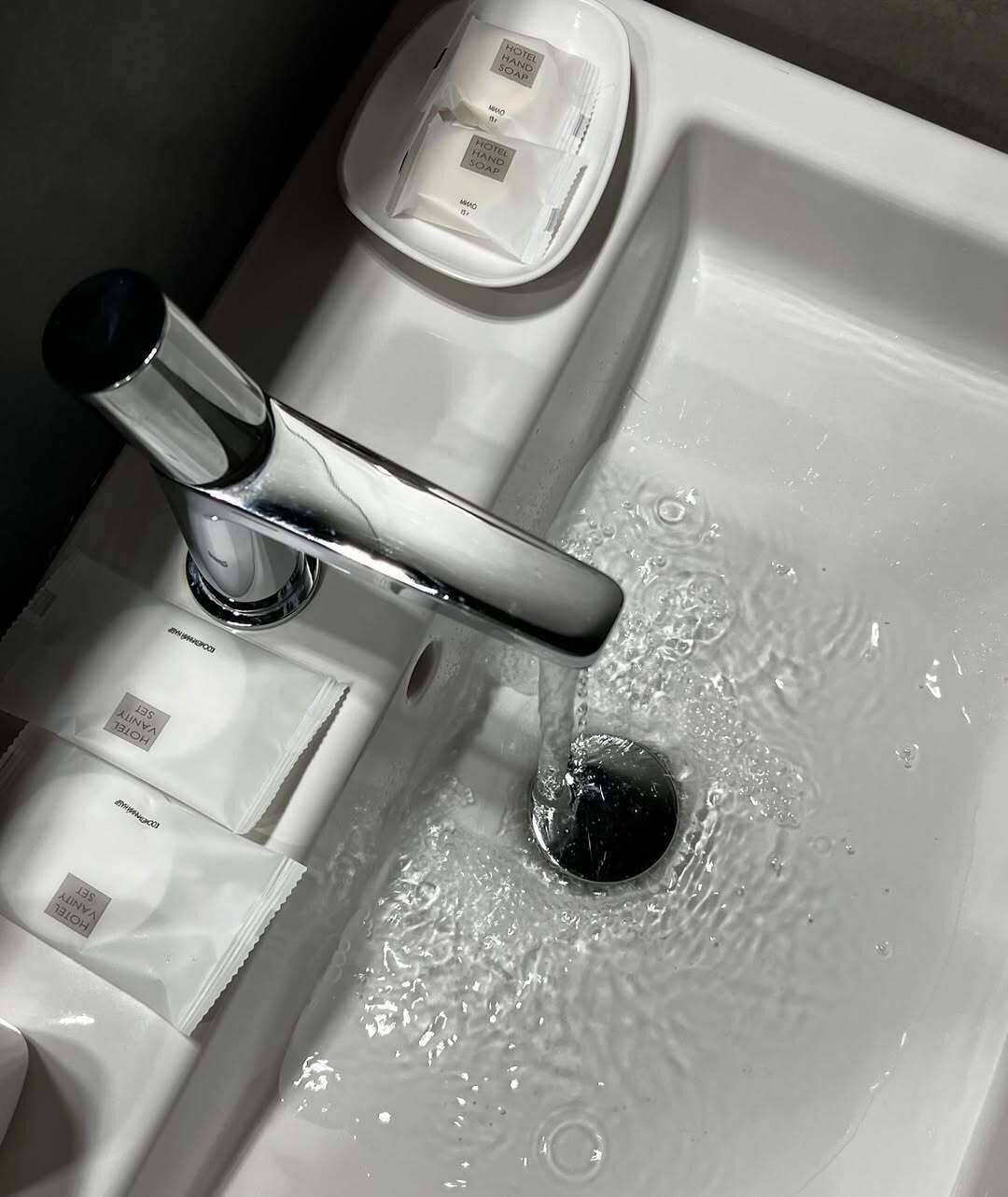 A hotel bathroom sink with a chrome faucet, soap dispenser, and a bottle of hand soap.