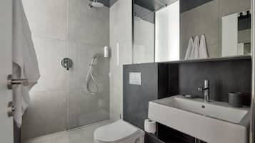 A modern bathroom with a walk-in shower, a toilet, and a sink with a mirror above.