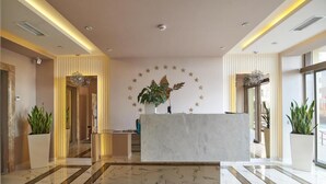 A modern hotel lobby with a marble reception desk, potted plants, and a star-patterned wall.
