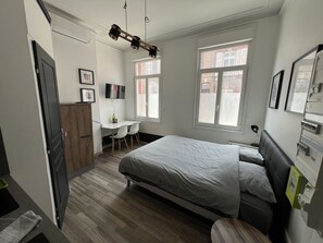 Ein Schlafzimmer mit Bett, Schreibtisch, Stuhl, Fernseher und Fenster.