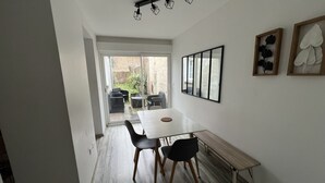 A dining area with a table and chairs, a bench, a sliding glass door leading to an outdoor patio, and a ceiling light fixture. - Côté Jardin AMIENS 4-6 P (Amiens)