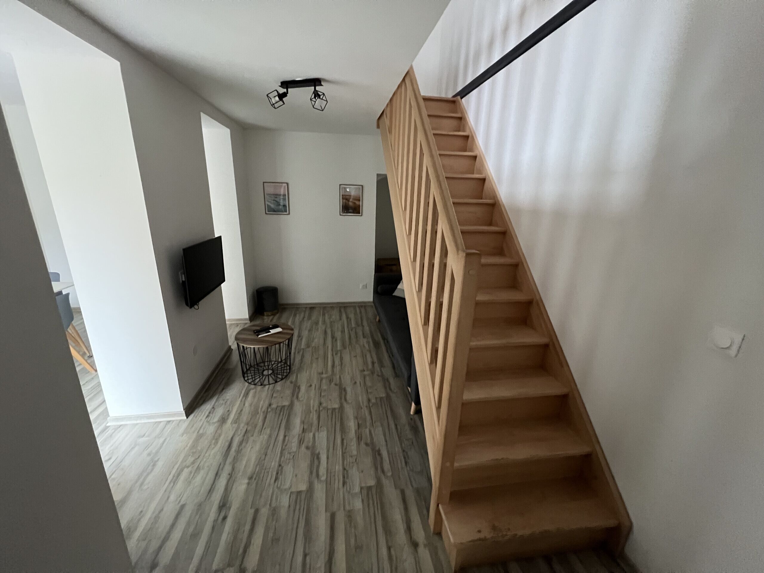 A modern interior with a wooden staircase, a flat-screen TV mounted on the wall, and a round coffee table with a remote control.