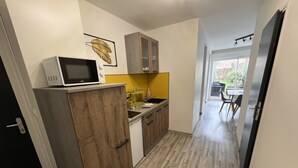 A compact kitchen with wooden cabinets, a microwave, and a yellow backsplash. - Côté Jardin AMIENS 4-6 P (Amiens)