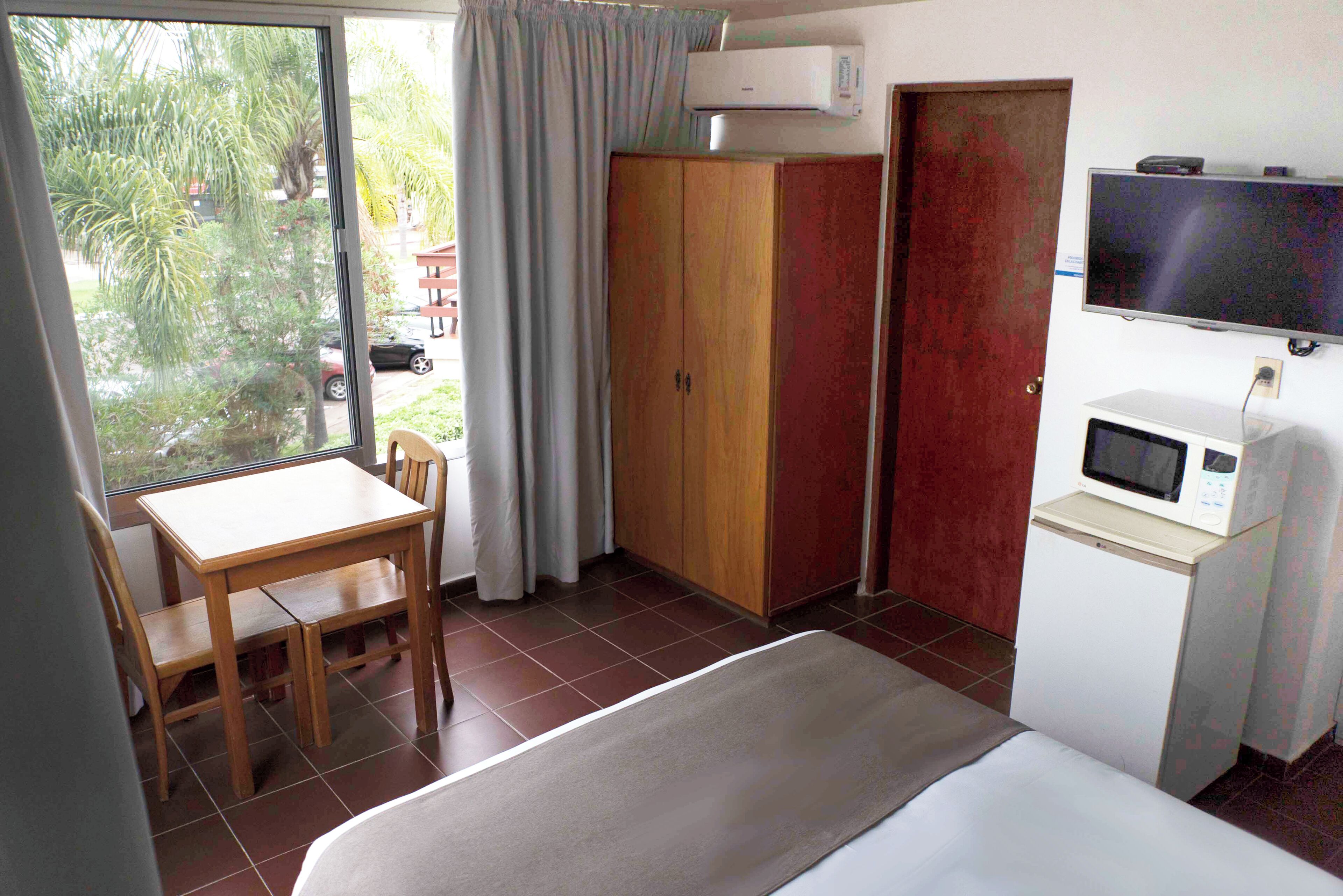 A hotel room with a bed, a desk with a chair, a wardrobe, a television, and a microwave.