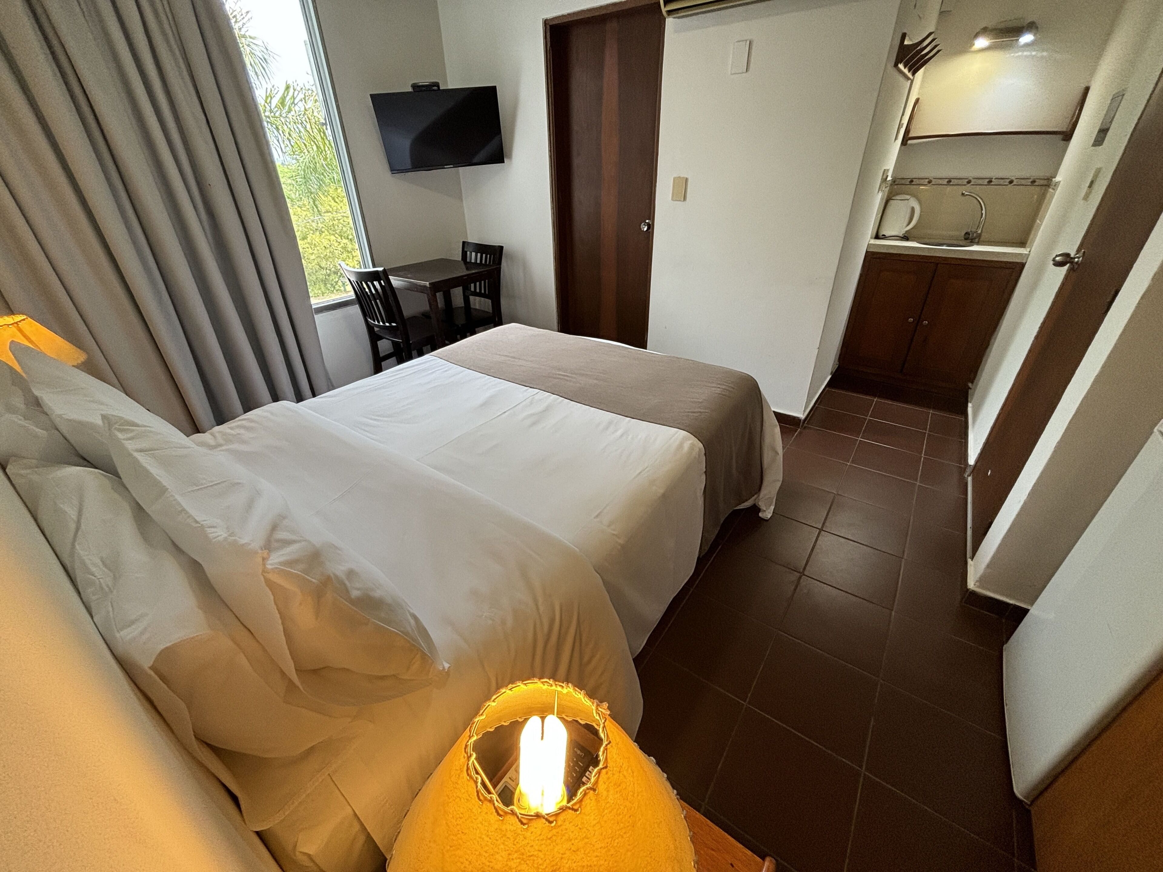 Een hotelkamer met twee bedden, een aan de muur bevestigde televisie, een klein tafeltje en een kitchenette.