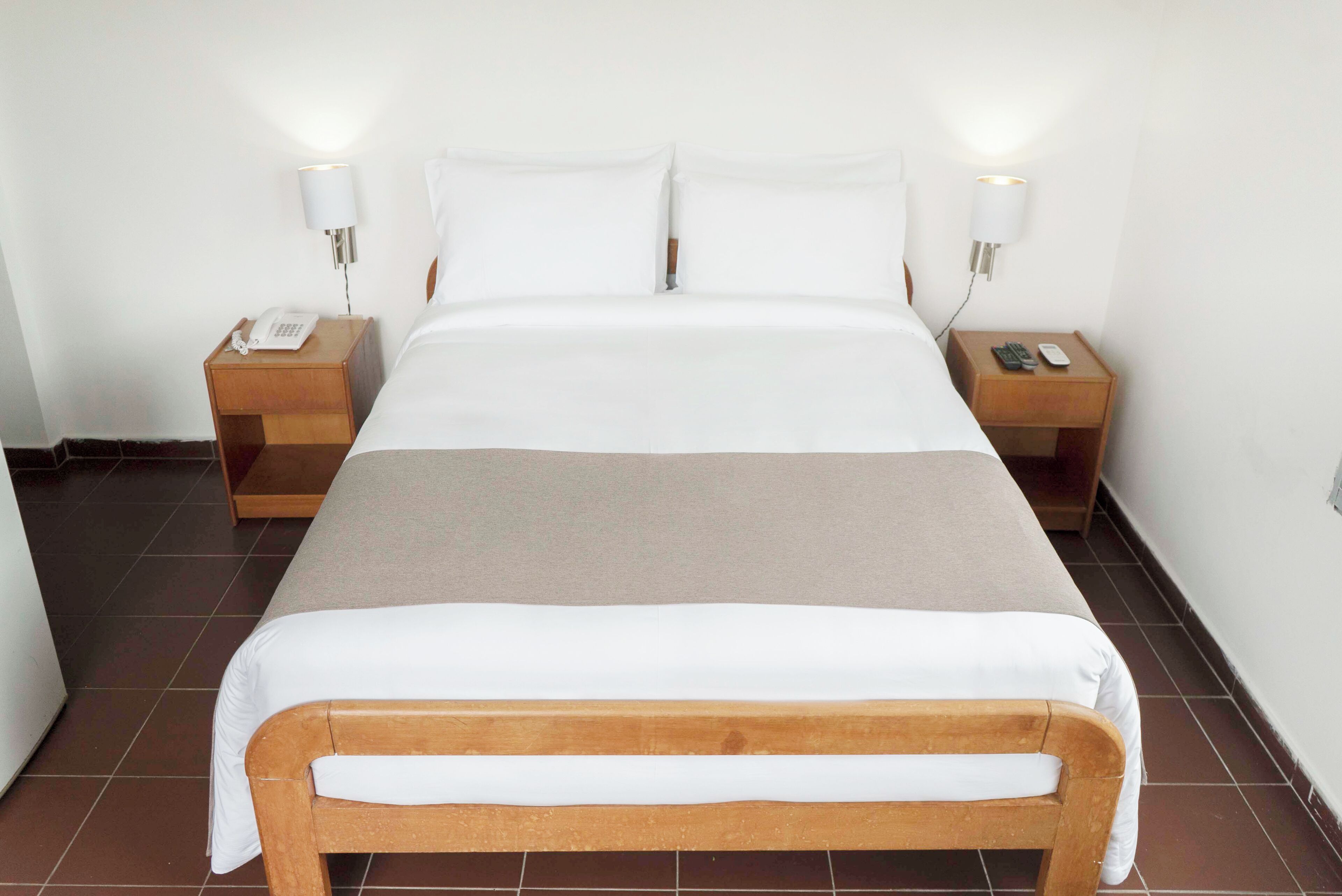 A neatly made bed with white linens, two bedside tables with lamps, and a wooden headboard.