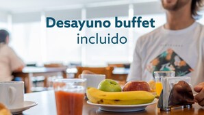 A buffet breakfast setting with a plate of fruits, a glass of juice, and a napkin dispenser.