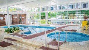 An indoor swimming pool with clear glass walls, steps leading into the pool, and a yellow chair in the foreground.