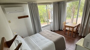 A hotel room with a bed, a desk with a telephone, a chair, and a window with curtains.
