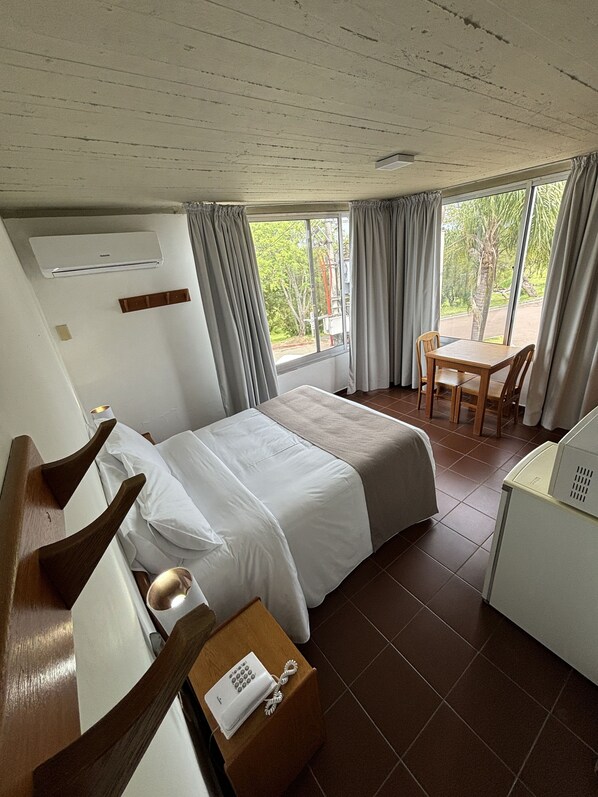A hotel room with a bed, a desk with a telephone, a chair, and a window with curtains.