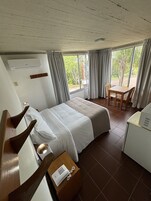 Una habitación de hotel con cama, escritorio, teléfono, silla y ventana con cortinas.