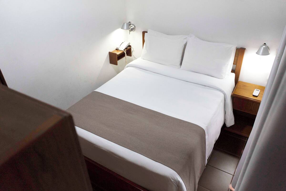 A neatly made bed with white linens, a bedside table with a lamp, and a phone.