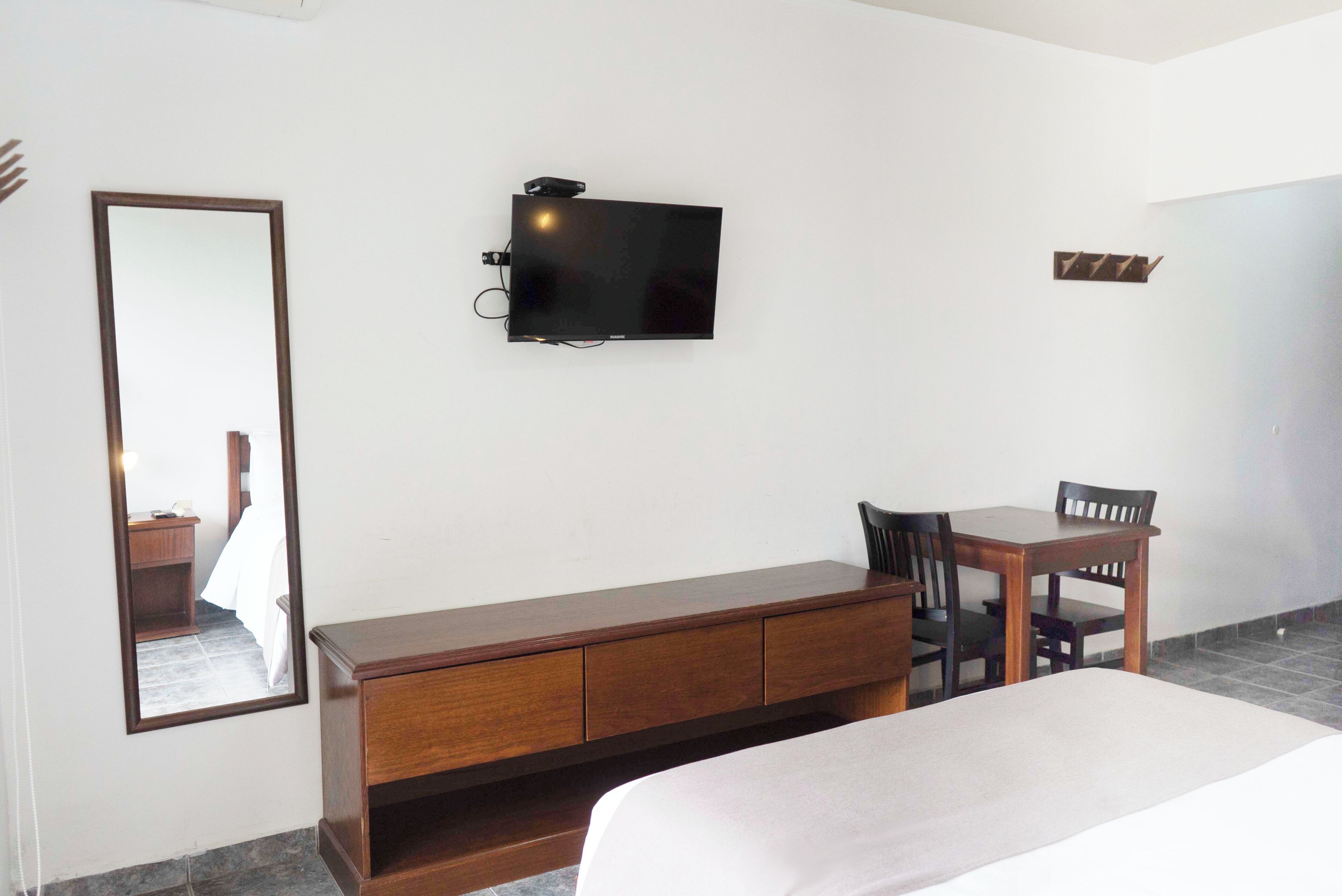 A hotel room with a bed, a wooden desk, a chair, a television, and a mirror.