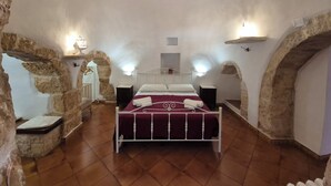 Een slaapkamer met een plafond van natuursteen, een bed met een rode spreideken en een wit metalen frame.